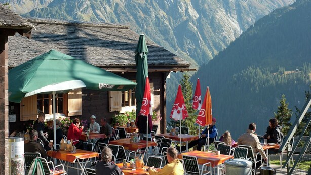 Un café en plein air, avec des tables et des chaises, entouré de montagnes.