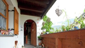 Une façade en bois, avec un chemin de pierre menant à une porte en bois, le tout agrémenté de plantes en pot et d’objets décoratifs.