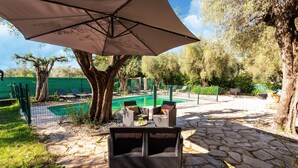 Un patio con piscina, mobiliario exterior y un paraguas grande.