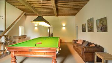 Une table de billard dans une pièce dotée d’un plafond en bois, d’un canapé en cuir marron et d’une petite table en bois.