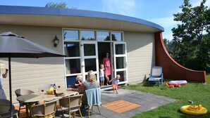 Una casa con un patio que cuenta con una mesa y sillas, una puerta corrediza de vidrio y un pequeño rincón de estar al aire libre con una silla y una mesa.