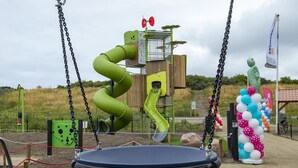 Un parque infantil con un tobogán verde, columpios y un arco decorativo de globos.