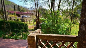 A stone bench with a lattice backrest, a paved walkway, and a view of a building with a red roof in a lush garden setting. - Dreamy Cottage in Trebbio with Pool (Trebbio)