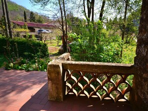 A stone bench with a lattice backrest, a paved walkway, and a view of a building with a red roof in a lush garden setting.