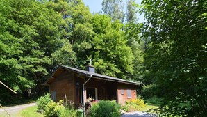 En rustik hytte omgivet af tæt skov, med en grussti, der fører til indgangen.
