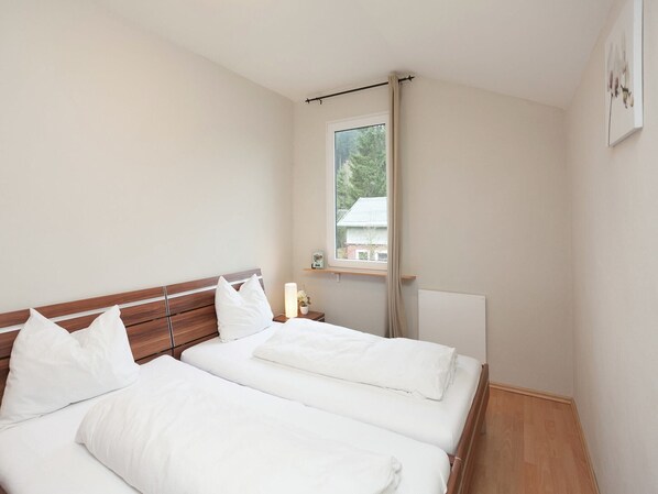 Une chambre avec deux lits, une fenêtre donnant sur un paysage verdoyant et une table de chevet avec une lampe.