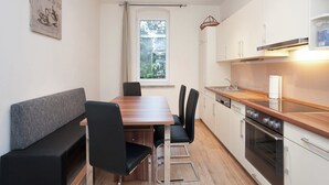 Une cuisine moderne avec des armoires blanches, un comptoir en bois et un four encastré. On y trouve une table à manger avec des chaises et un banc. Une fenêtre laisse entrer la lumière naturelle, et un tableau encadré est accroché au mur.