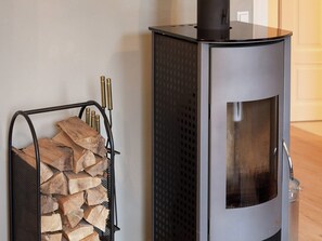 Un poêle à bois moderne doté d’une porte en verre, placé à côté d’un support métallique où est entreposé le bois de chauffage.