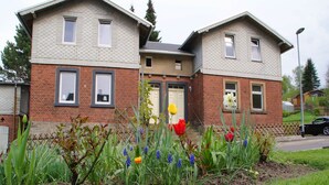 Une maison à deux étages avec une façade en briques et un petit jardin agrémenté de tulipes et d’autres fleurs.