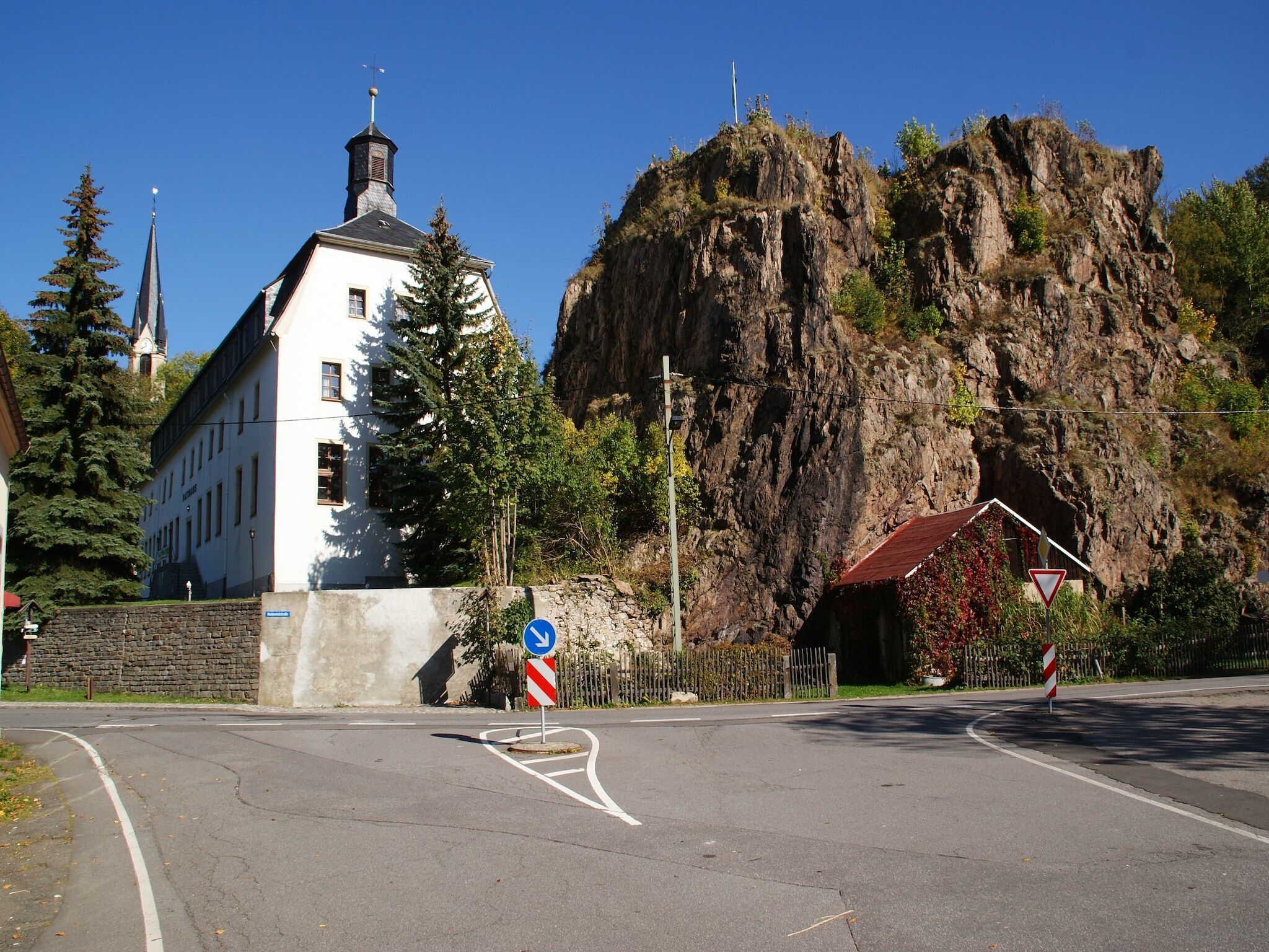 En bygning med en hvid facade og et stejlt tag, beliggende ved siden af en klippe.