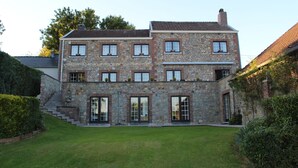 A stone building with a two-story layout, featuring multiple windows and a staircase leading to the entrance.