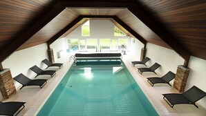 An indoor swimming pool with a sloped ceiling and multiple lounge chairs along the sides.