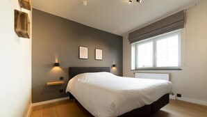 A modern bedroom with a large bed, bedside lamps, a window with curtains, and a wall-mounted shelf.