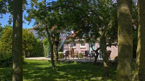 En gårdsplads med en murstensbygning, udendørs siddepladser og træer.