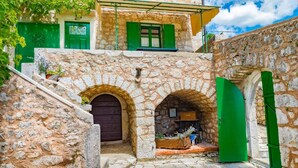 A stone building with green doors and windows, a staircase, and a small garden area.