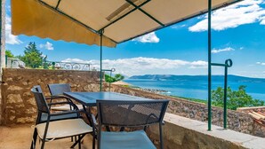 An outdoor patio with a table and chairs, overlooking a scenic view of the sea and mountains.
