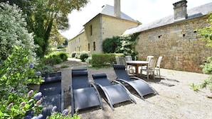 A stone building with a garden area featuring lounge chairs and a table. - Elegant Manor Retreat Normandy (Lantheuil)
