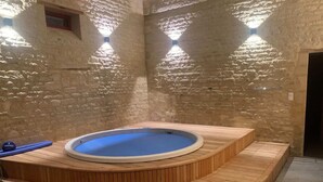 A hot tub with a wooden deck, set against a stone wall with a small window. - Elegant Manor Retreat Normandy (Lantheuil)