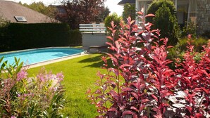 A swimming pool surrounded by a well-maintained lawn and various plants. - Spacious Home with Garden (Waimes)