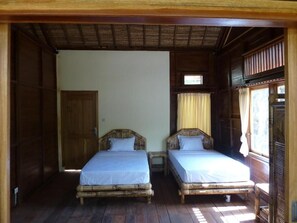 Une pièce avec deux lits en bois, une fenêtre avec des rideaux et une porte en bois.