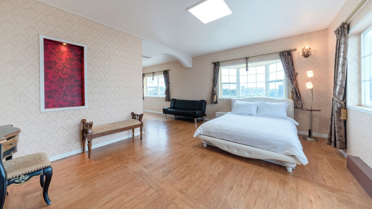 A spacious bedroom with a large bed, a bench, a desk, and a floor lamp.