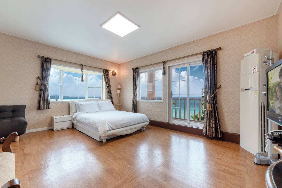 A hotel room with a bed, a TV, a sofa, and a balcony with a view of the sea.
