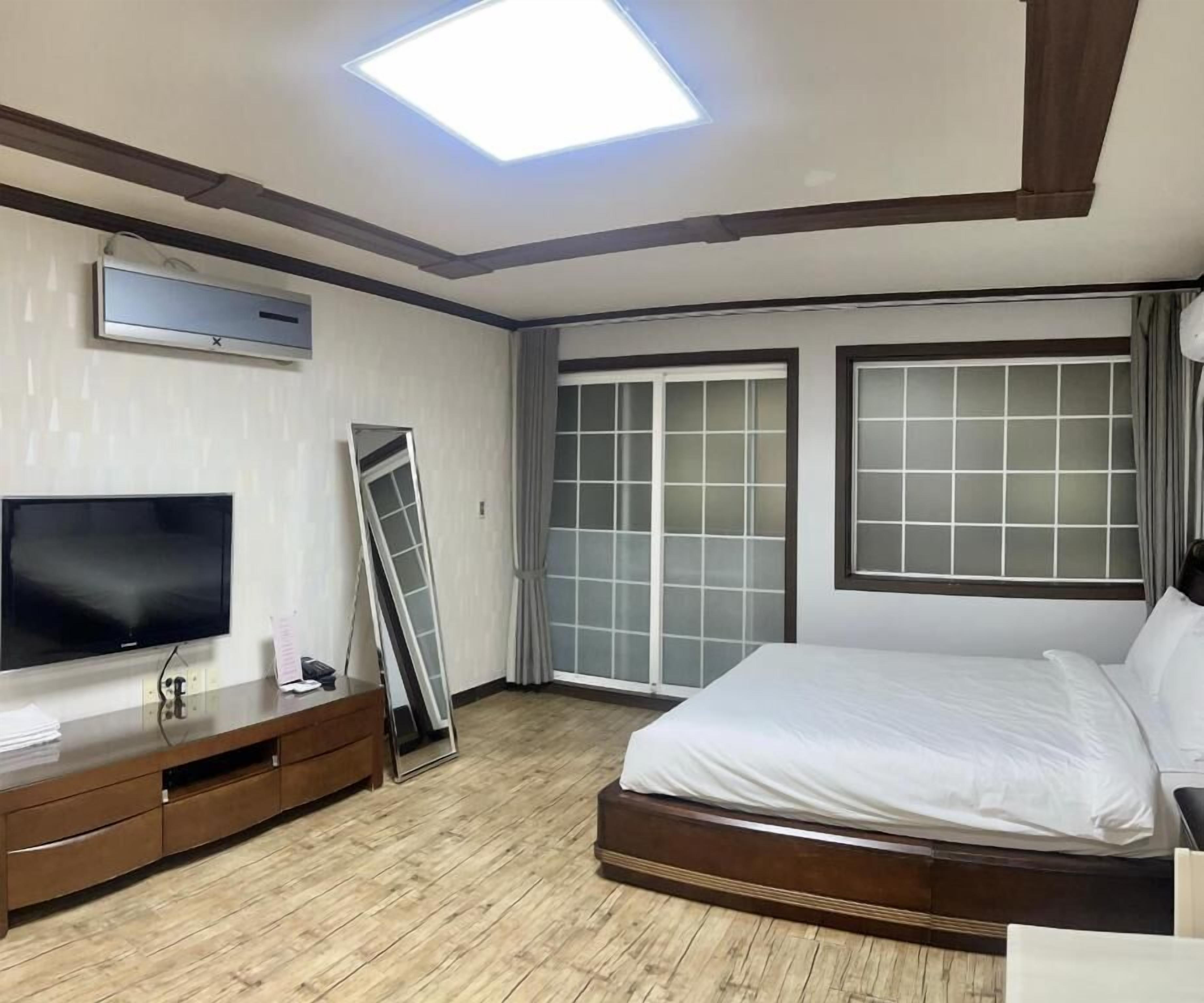 A modern hotel room with a large bed, a flat-screen TV, a ceiling light, and a sliding glass door.