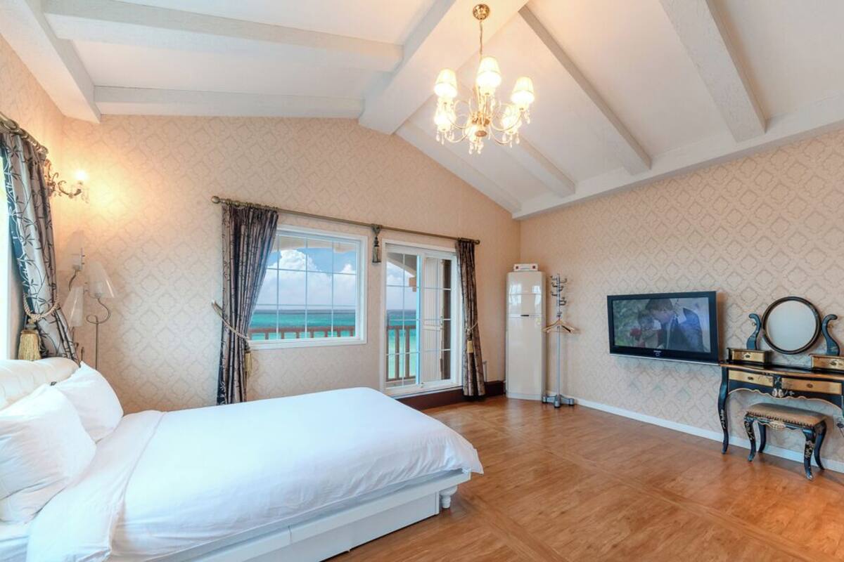 A bedroom with a large bed, a TV, a dresser, and a balcony with a view.