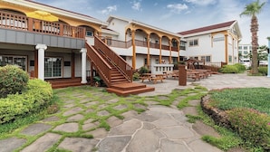 Un hotel con un espacio exterior cubierto, una escalera que lleva a un balcón y un patio con mesas y sillas.