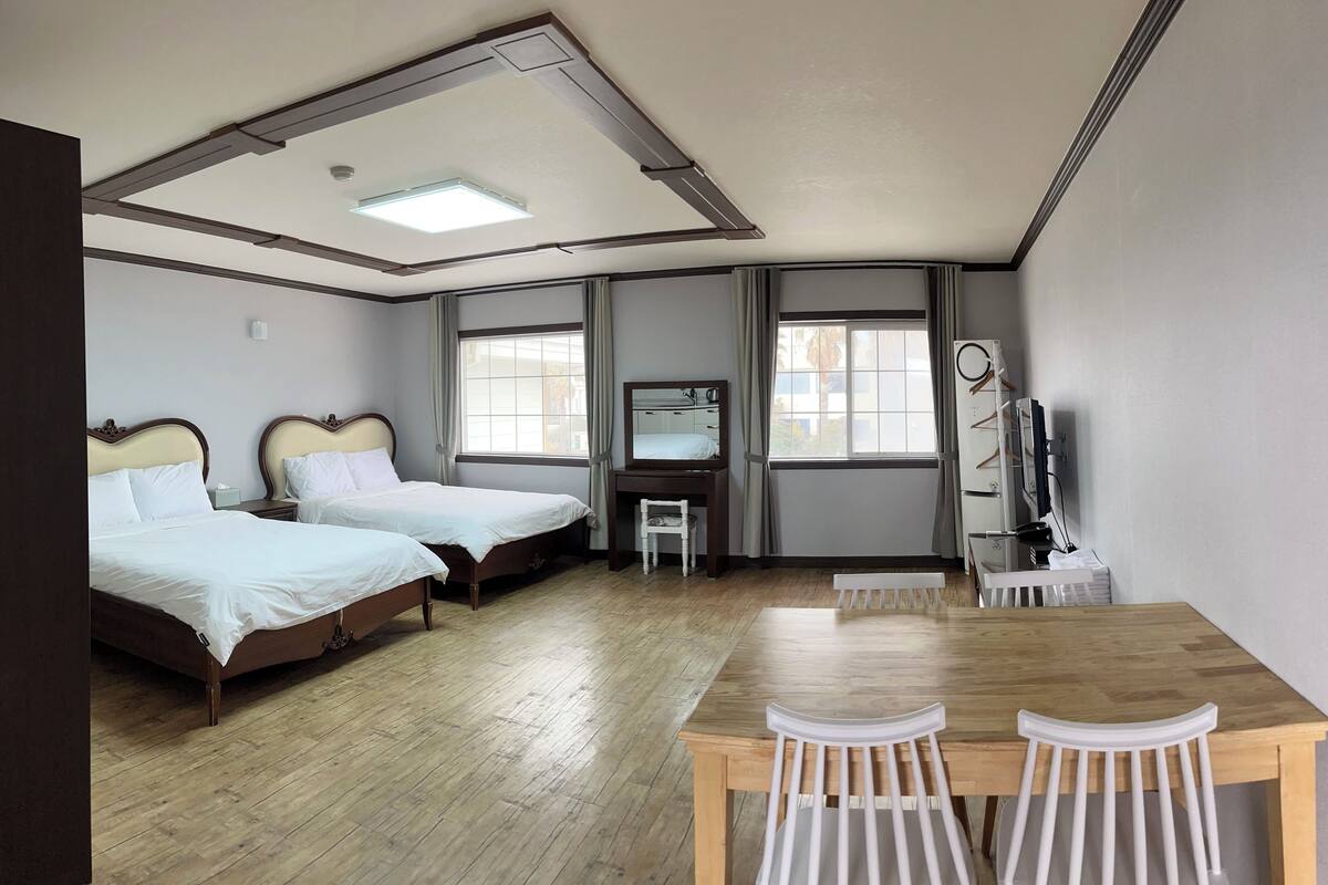 A hotel room with two beds, a desk, a chair, a mirror, and a window.