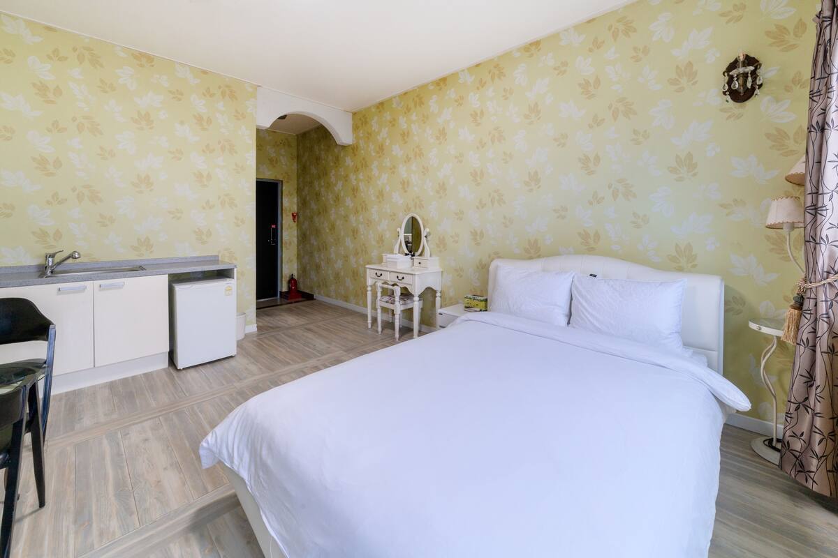 A hotel room with a bed, a desk with a mirror, a chair, and a small refrigerator.
