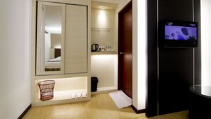 Une chambre d’hôtel dotée d’un grand miroir, d’une télévision, d’un petit coin salon et d’une étagère contenant des articles de toilette.
