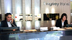 Un comptoir d’accueil au Kingsley Hotel, doté d’un design moderne, avec une cloison en verre et un panneau en bois sur lequel figure le nom de l’hôtel.