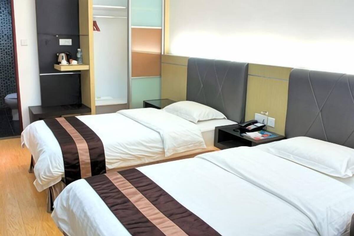 Una habitación de hotel con dos camas, una mesita de noche con teléfono y un armario con espejo.