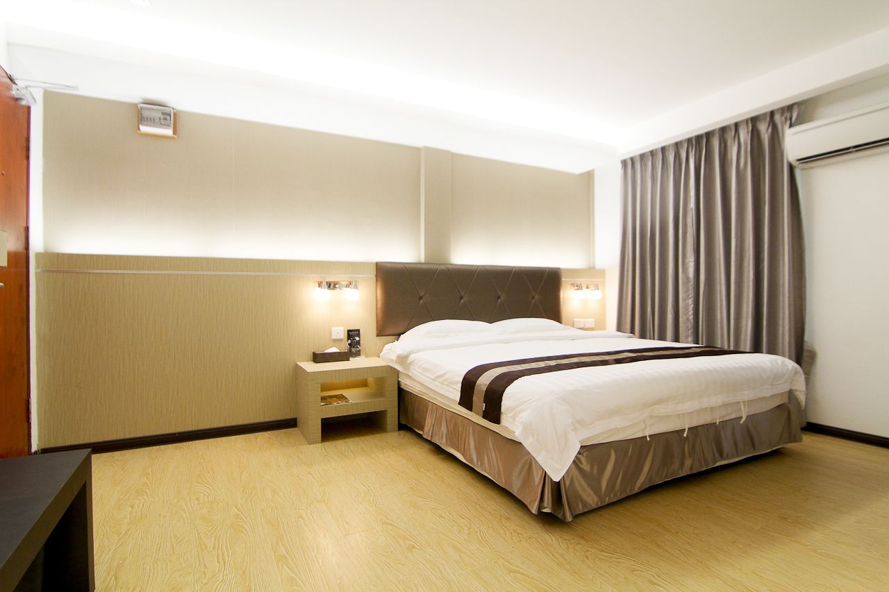 A hotel room with a large bed, bedside tables, a headboard, and a window with curtains.