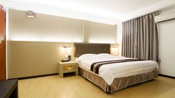 A hotel room with a large bed, bedside tables, a headboard, and a window with curtains.