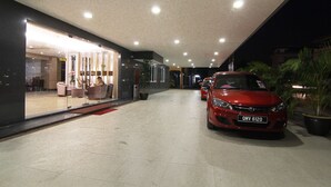Un bâtiment moderne avec une façade en verre, une voiture rouge garée devant, et un intérieur bien éclairé.