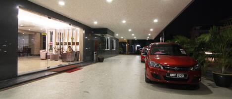 Um edifício moderno com fachada de vidro, um carro vermelho estacionado na frente e um interior bem iluminado.