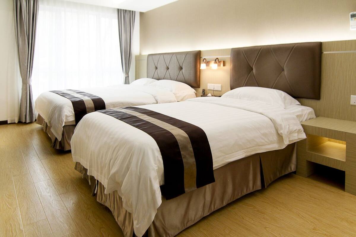 Habitación de hotel con dos camas, suelo de madera, cabecero moderno y mesita de noche con lámpara.