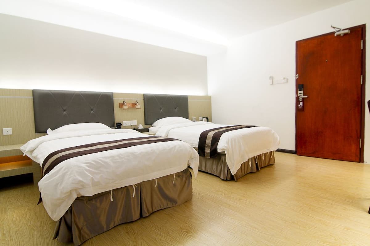Habitación de hotel con dos camas, una puerta de madera y una mesita de noche pequeña con una lámpara.