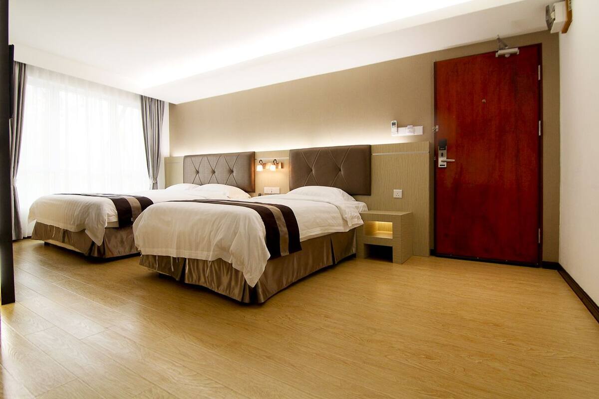 Habitación de hotel con dos camas, piso de madera, puerta roja y una mesita de noche con lámpara.