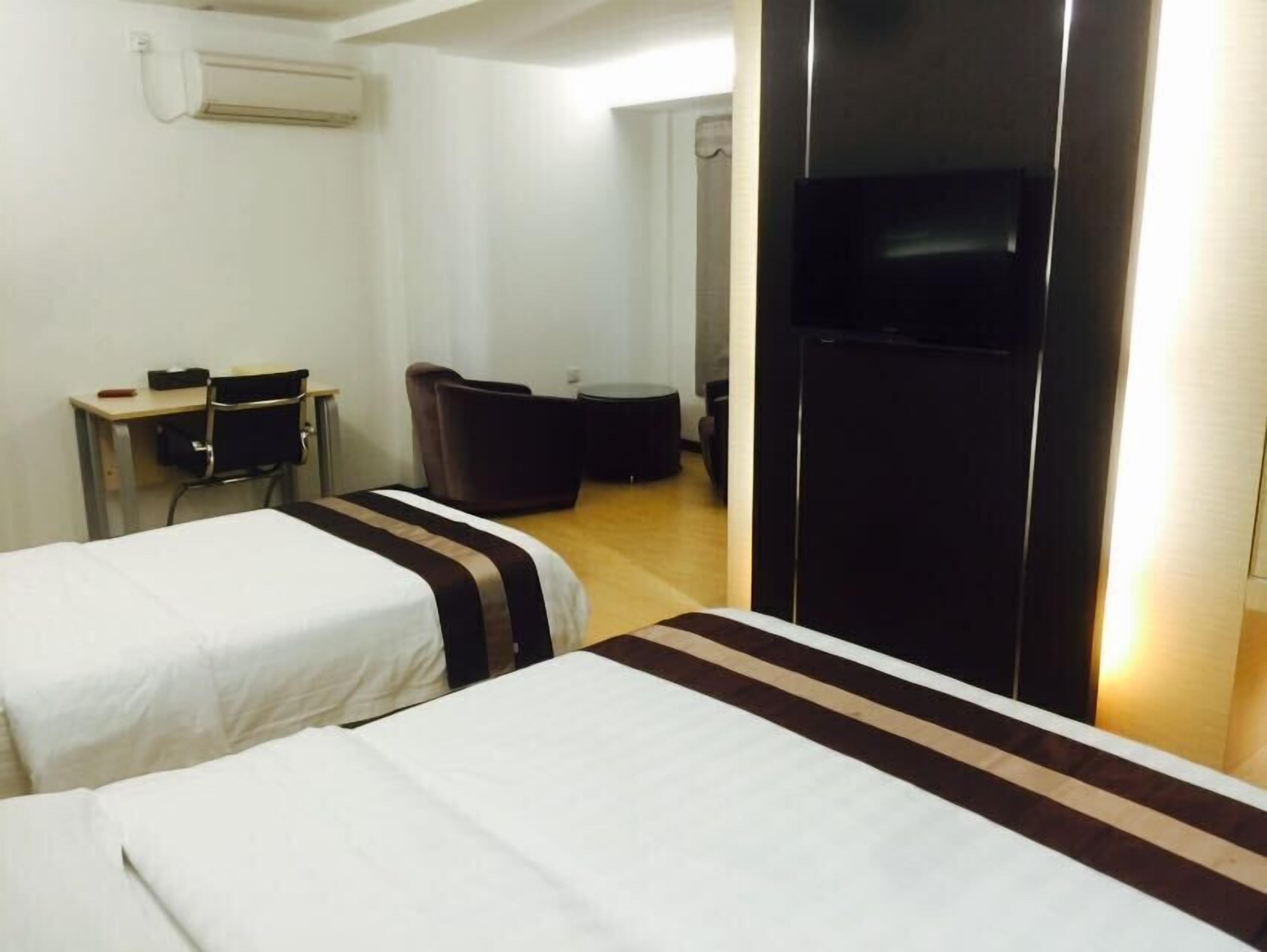 A hotel room with two beds, a desk, a chair, a sofa, and a TV.