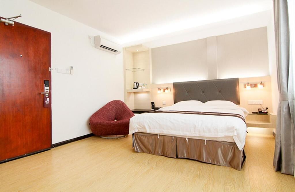 A hotel room with a large bed, a red chair, a wooden floor, a wooden door, and a wall-mounted air conditioner.
