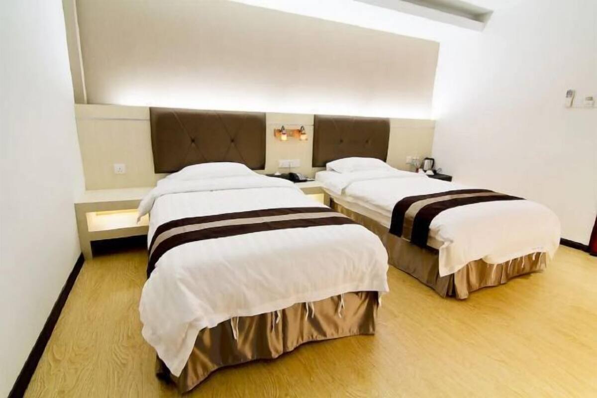Habitación de hotel con dos camas, cada una con cabecero y mesitas de noche.