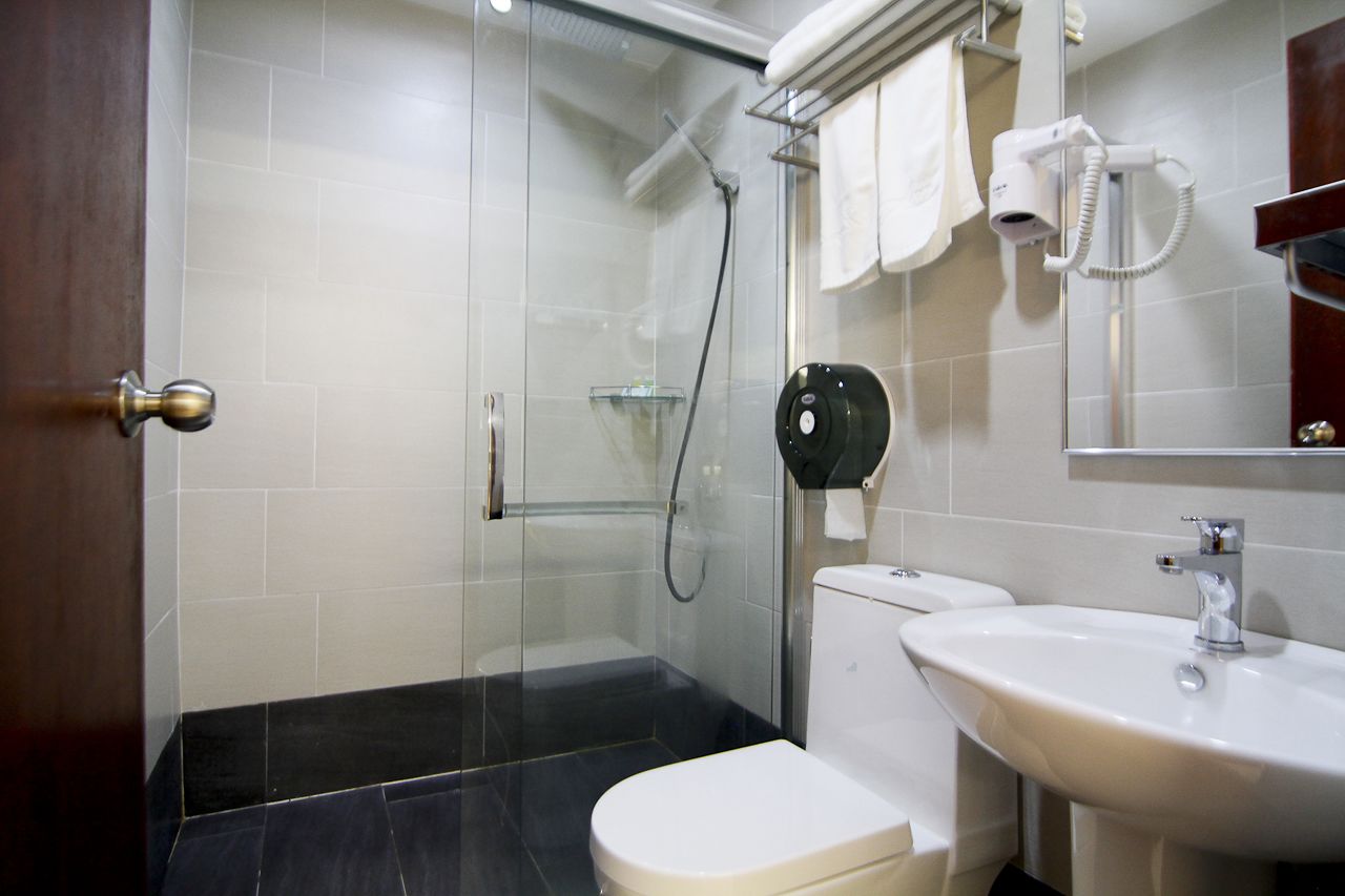 Un baño moderno con cabina de ducha de vidrio, inodoro blanco, lavamanos y secador de pelo montado en la pared.