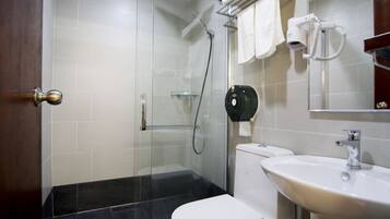Un baño moderno con cabina de ducha de vidrio, inodoro blanco, lavamanos y secador de pelo montado en la pared.