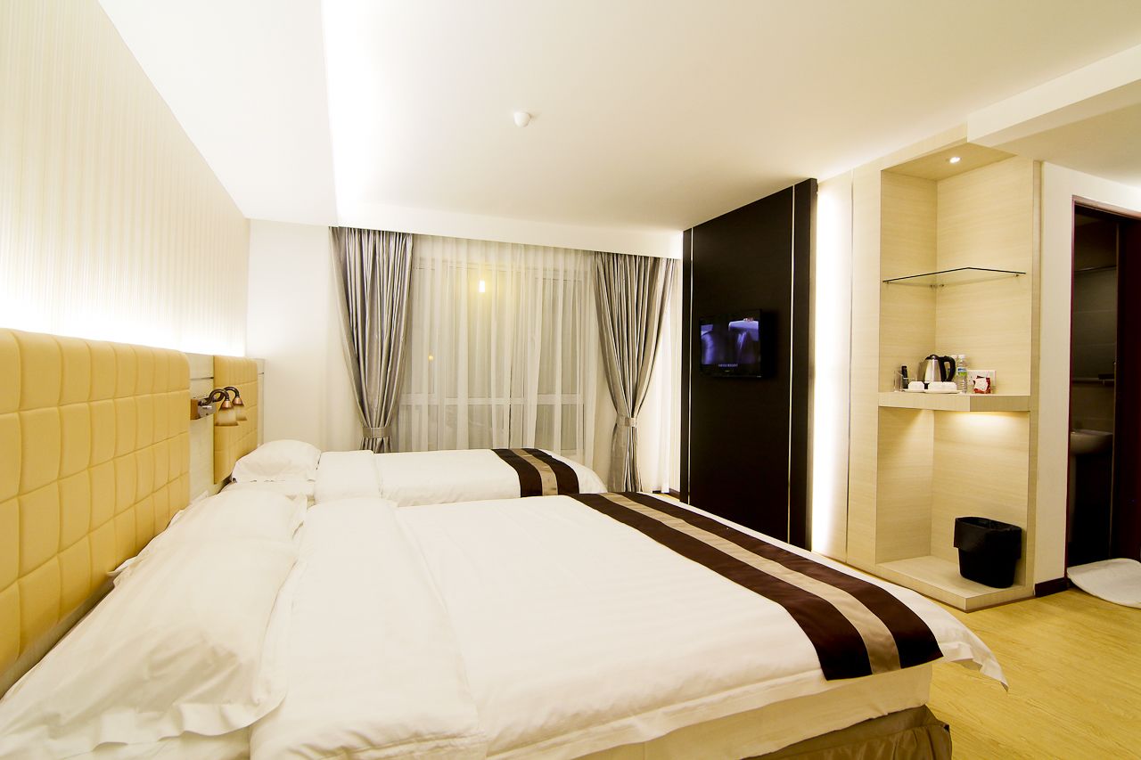 Habitación de hotel con dos camas, un televisor, un pequeño estante con artículos de aseo y una puerta al baño.
