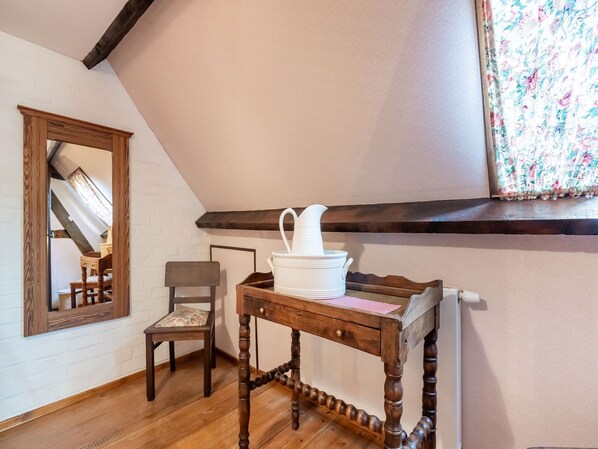 A room with a wooden table, a chair, a mirror, and a window with floral curtains.