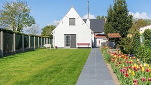 A white house with a grey door and a chimney, a fenced yard with a sheep, and a garden with tulips. - Farmhouse in Beveren near Beach & Garden (Beveren a/D Ijzer)