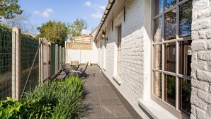 A narrow outdoor corridor with a tiled floor, a white brick wall, and a metal gate on one side. - Farmhouse in Beveren near Beach & Garden (Beveren a/D Ijzer)